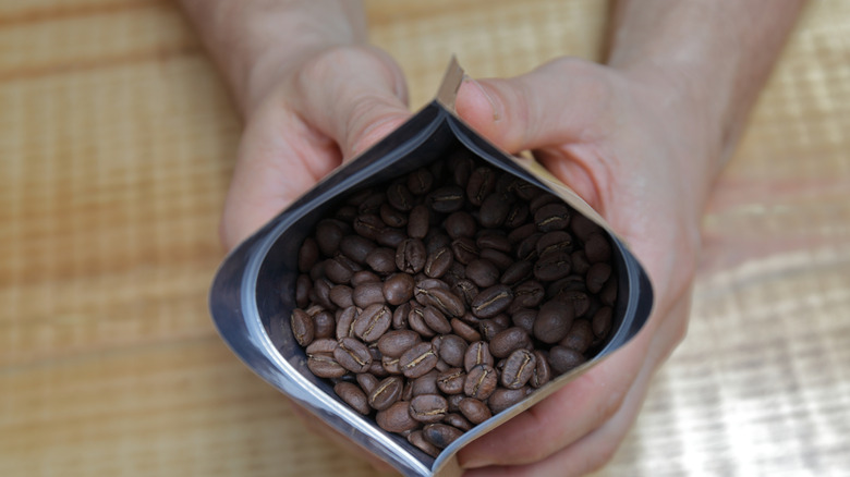 Close-up of hands holding an opened bag filled with freshly roasted coffee beans.