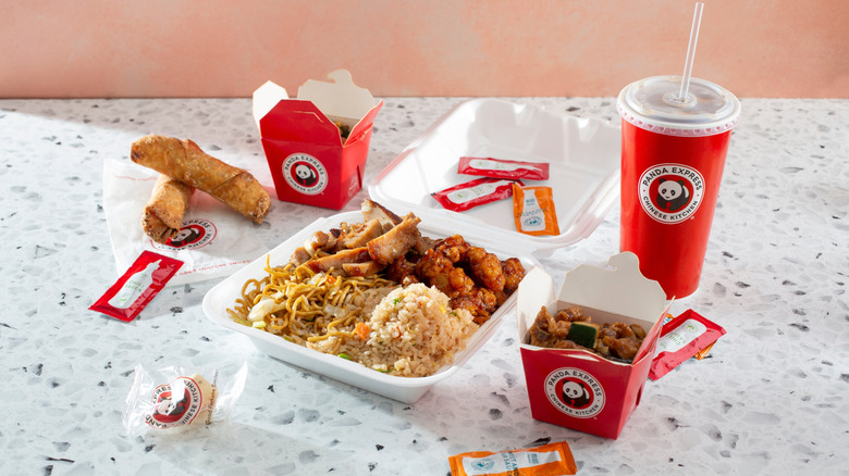 Box of Panda Express food surrounded by sauces, boxes, and a drink