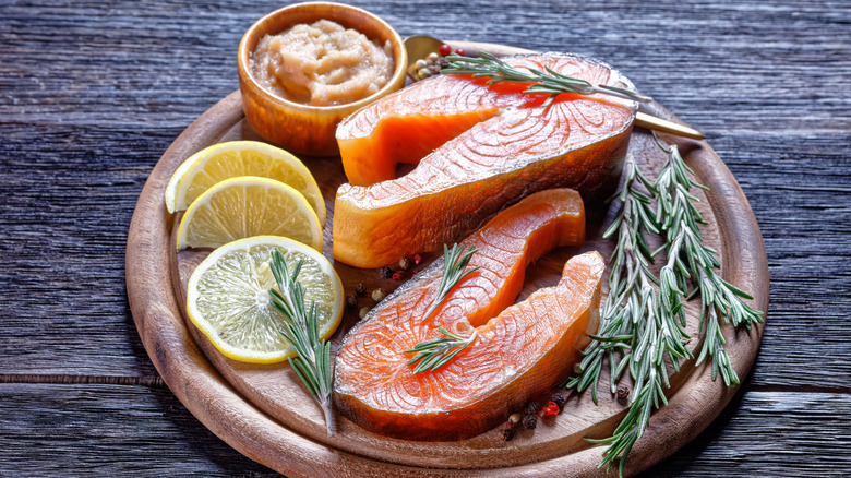 Smoked Arctic char rests surrounded by herbs and lemon slices on a wooden plate.