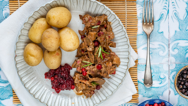 A plate of reindeer stew, potatoes, and berries.