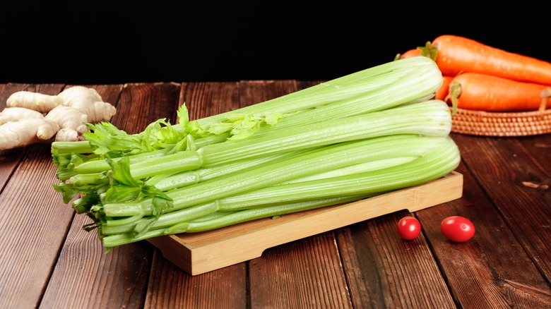 A stack of celery on a wooden cutting board with other veggies in the background