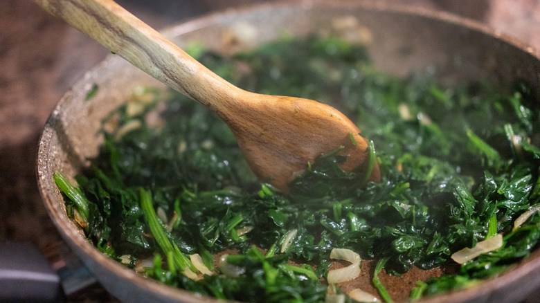 A wooden spoon stirring sautéed spinach and onion