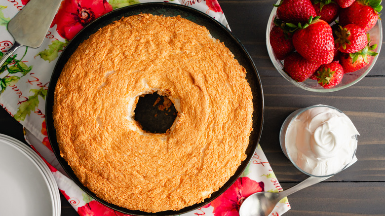 plain angel food cake in pan surrounded by strawberries and whipped cream
