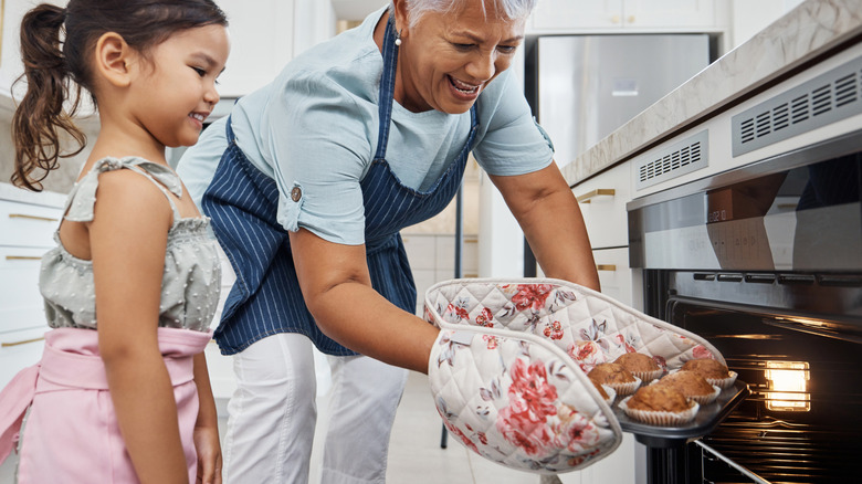 Grandma and grand daughter pulling muffins out of oven