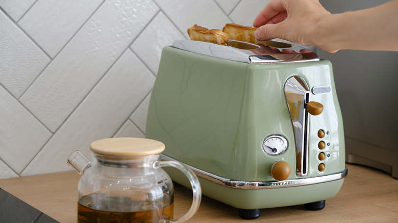 Woman using a mint green toaster to prepare sandwiches for breakfast