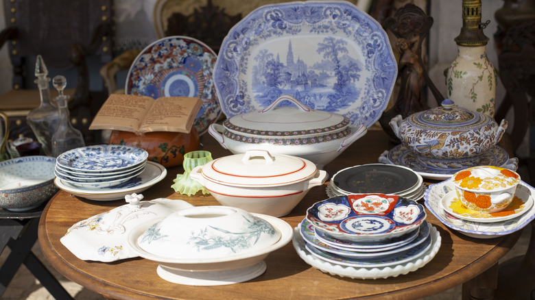 An assortment of vintage plates, bowls, and platters in a flea market on a wooden table