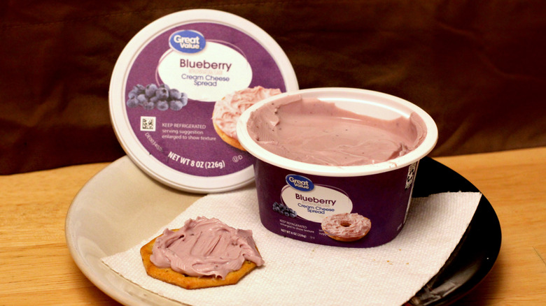 A container of Great Value Blueberry cream cheese spread on a plate beside a cracker spread with the cream cheese