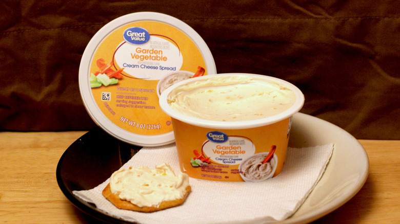 A container of Great Value Garden Vegetable cream cheese spread on a plate beside a cracker spread with the cream cheese