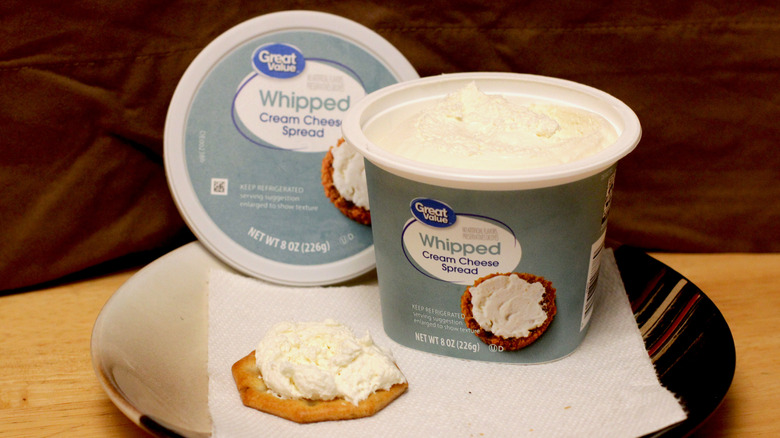 A brick of Great Value plain whipped cream cheese on a plate beside a cracker spread with the cream cheese and the box it came in