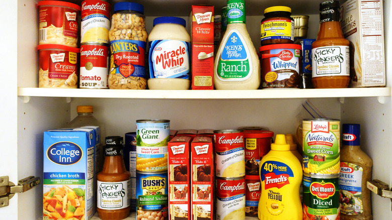 A pantry shelf filled with a variety of items such as bbq sauce, salad dressing, and canned vegetables.