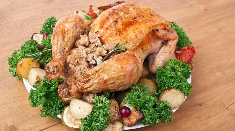 Roasted chicken with stuffing on a plate decorated with roasted vegetables and herbs.