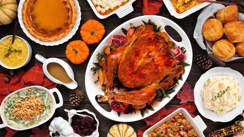 Festive Thanksgiving table spread with whole roasted turkey, rolls, gravy, pies, and a variety of casseroles.