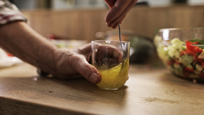 Hands stirring a vinaigrette in a glass jar