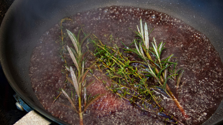 A pan being deglazed with alcohol and herbs