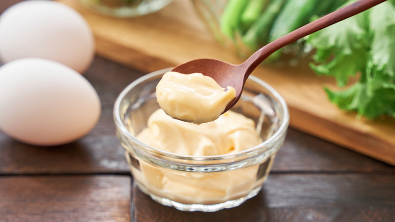Spoon full of mayonnaise over a bowl next to two eggs