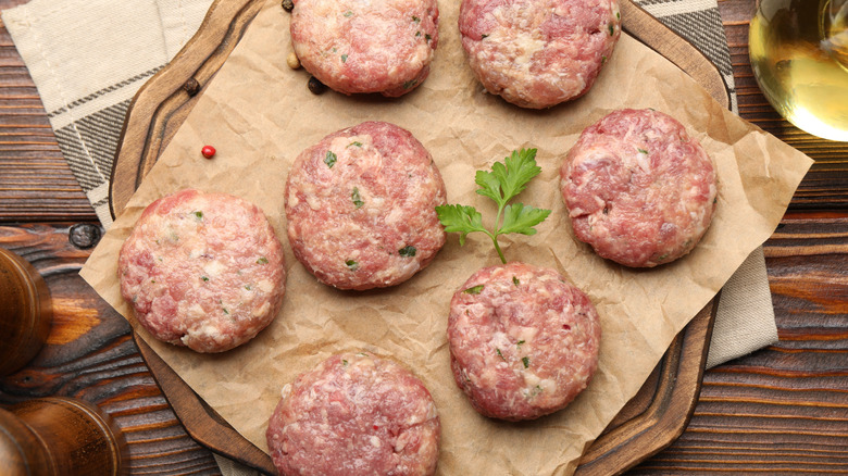 Raw meat patties with parsley and peppercorns on a wooden table