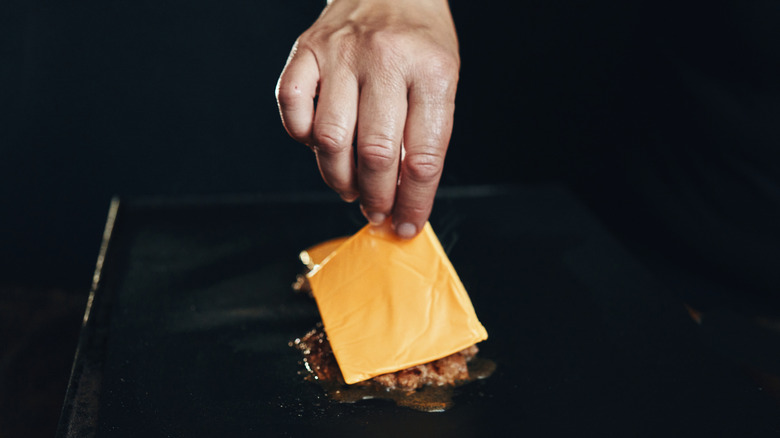Hand laying a slice of cheese onto a patty