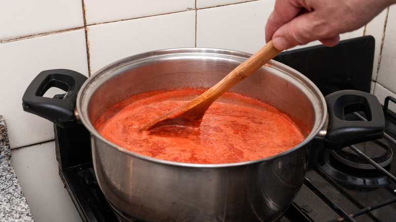 Hand stirring simmering tomato sauce with a wooden spoon