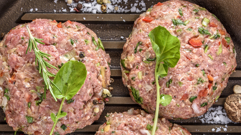 Top view of two raw hamburger patties with spices in a cast iron pan