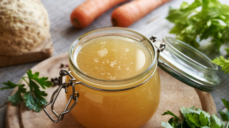 A glass jar of broth sitting on a wooden cutting board