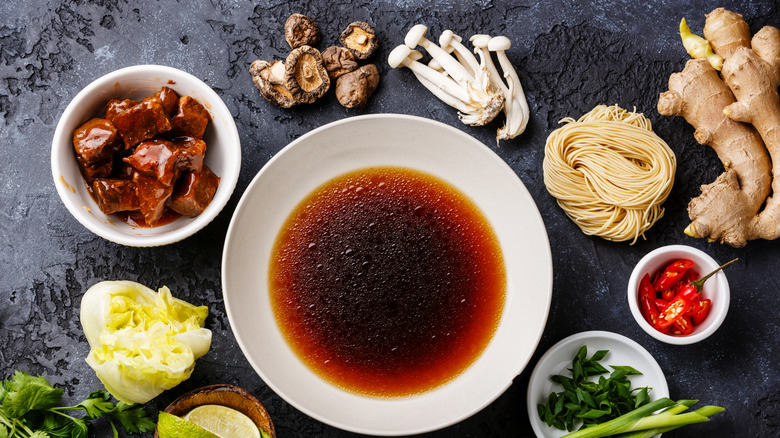Various Asian-inspired ingredients in bowls on a table, including mushrooms, cabbage, fresh ginger root, chili peppers, fish sauce, and fresh herbs
