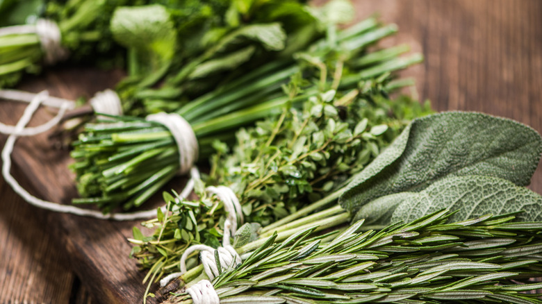 Freshly cut bunches of herbs, like sage, thyme, and chives, on a wood table