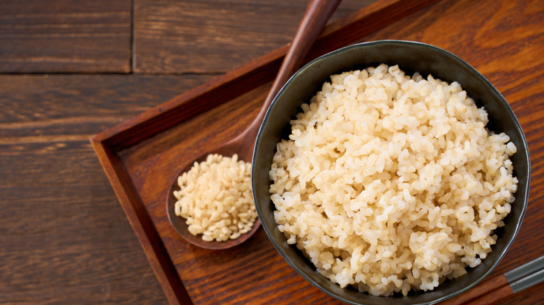 A bowl and spoon of brown rice on a wooden tray