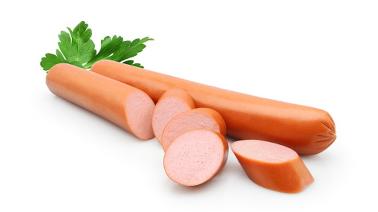 Fresh frankfurter sausages whole and sliced, with parsley leaf isolated on white background