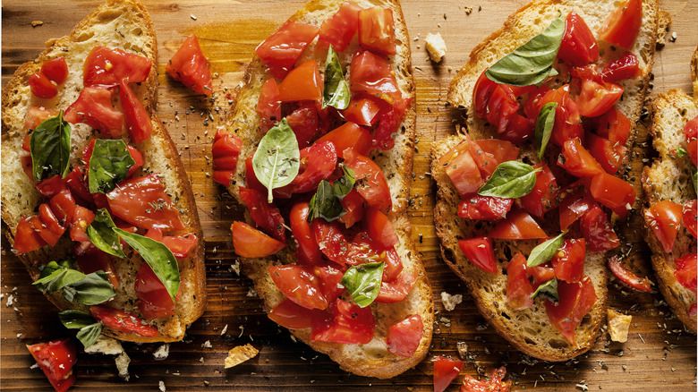 Crusty bread on a rustic wooden cutting board topped with diced tomatoes and fresh basil.