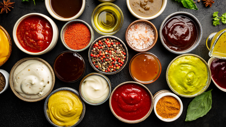 Multiple small bowls filled with different colored sauces and spices on a black countertop.