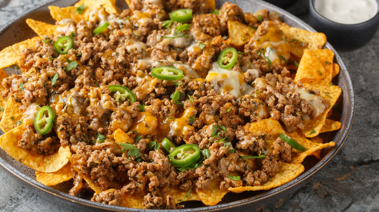 Platter of corn chips tops with taco meat, sliced jalapeños and melted cheese.