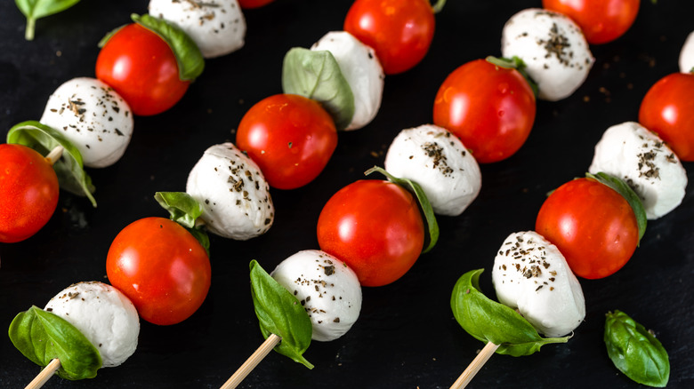 Skewers of cherry tomatoes, basil leaves, and fresh mozzarella with a solid blackk background.