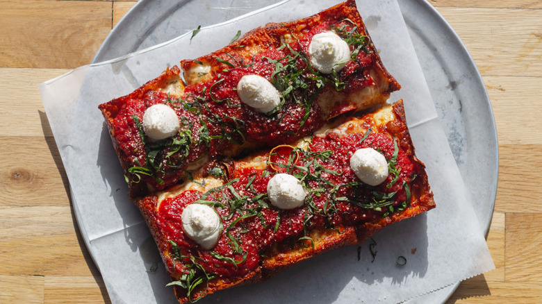Six square slices of Detroit-style pizza withe topped with marinara, fresh herbs, and a dallop of ricotta cheese.