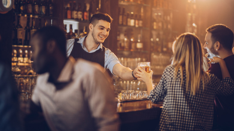 A bartender smiling, while handing a drink to a couple sitting at the bar.