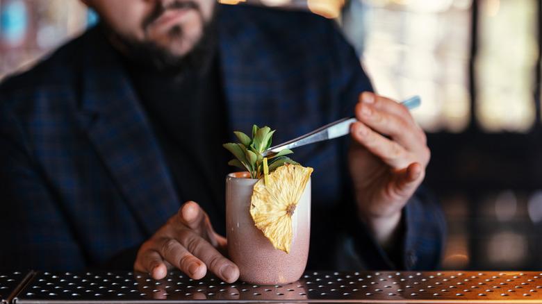 A bartender adding garnish to the top of a cocktail at a bar.
