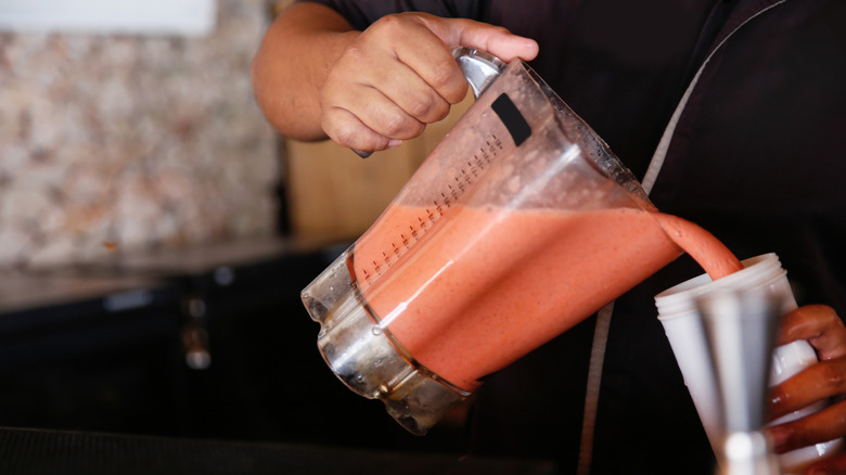A bartender pours a smoothie from a blender into a white plastic cup.