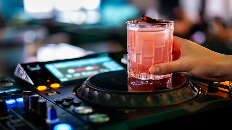 A hand holds a pink cocktail, which rests on a sound system.