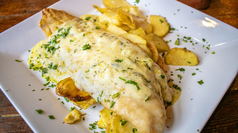 Close up of fried fish and potatoes on white plate, smothered in cheese sauce