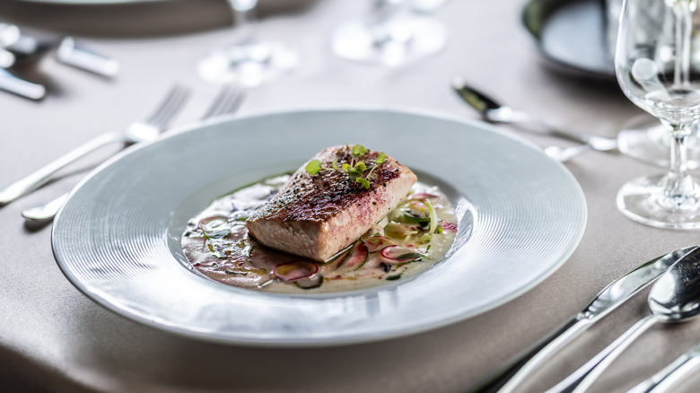 Fillet of salmon with herbs and white sauce on formal restaurant table