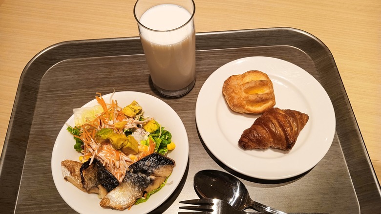 Breakfast tray with glass of milk, salmon, salad, and pastries