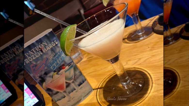 A frozen margarita in a martini glass with a lime wedge garnish