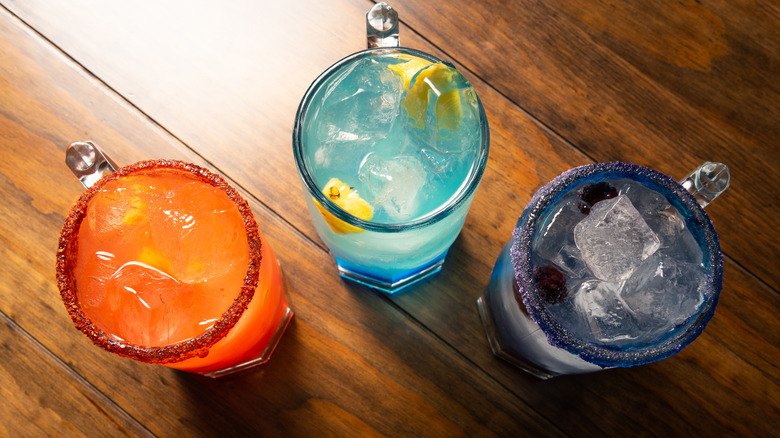 Overhead view of three different colored cocktails on a wooden table