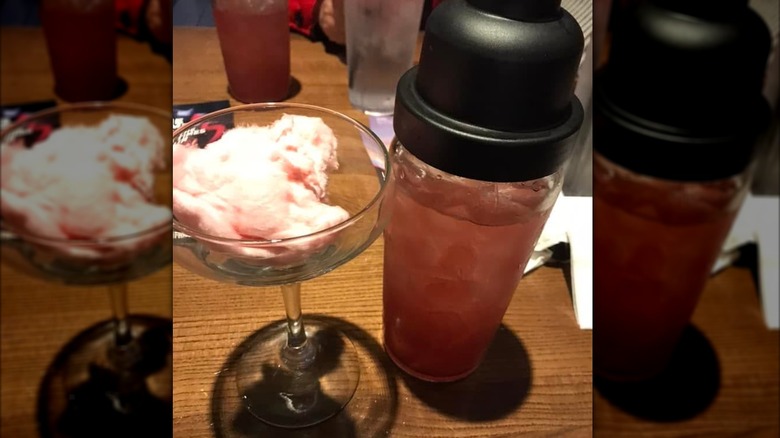 A martini glass filled with cotton candy next to a full plastic cocktail shaker on a wooden table
