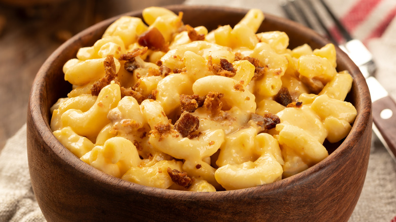 A wooden bowl of mac and cheese topped with bacon bits