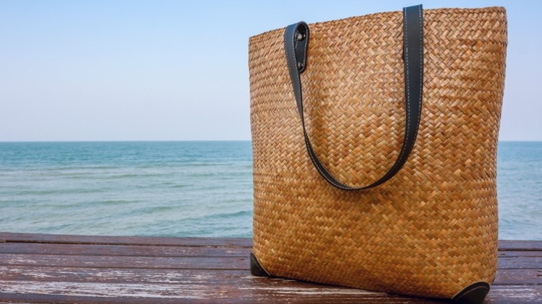 a woven bamboo bag with black accents on a wooden surface with the ocean in the background