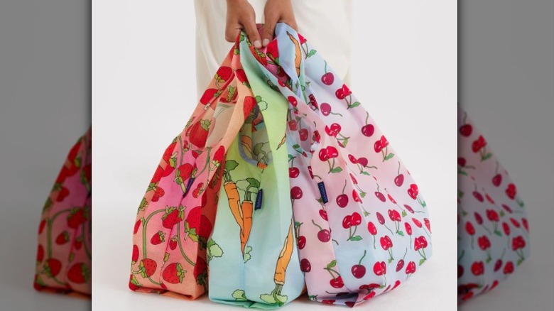 A person holds three Baggu reusable nylon bags in cherry, carrot, and strawberry prints