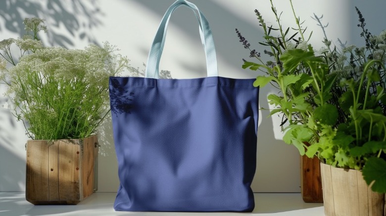 dark blue tote bag with light blue strap sits between two potted plants