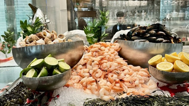 A pile of cooked shrimp on ice at Bacchanal Buffet surrounded by stainless steel bowls of citrus wedges and shellfish