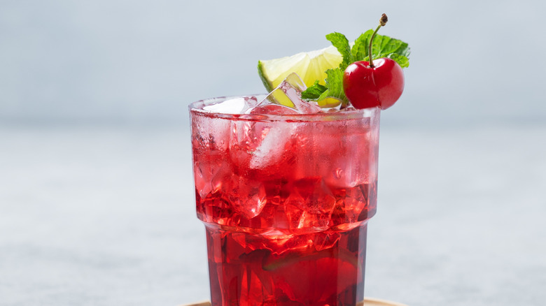 A red drink with cherry, lime, and mint garnishes