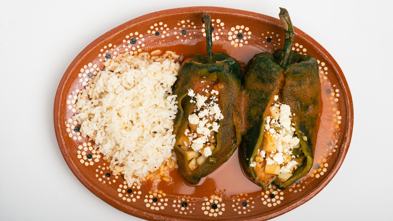Stuffed peppers and rice topped with queso fresco on a decorative earthenware plate